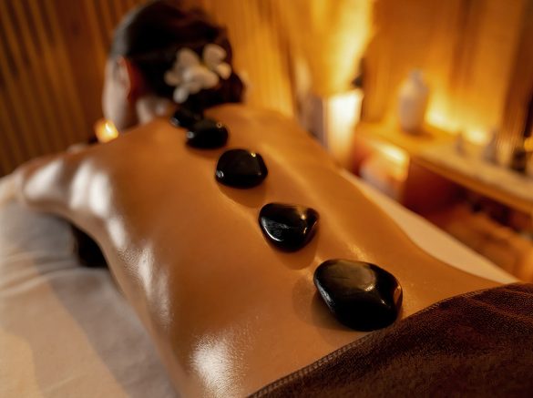 Hot stone massage at spa salon in luxury resort with warm candle light, blissful woman customer enjoying spa basalt stone massage glide over body with soothing warmth. Quiescent